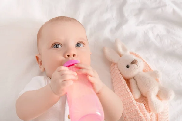 Portrait of cute little baby drinking milk from bottle on bed — Stock Photo, Image