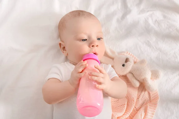 Portrait of cute little baby drinking milk from bottle on bed — Stock Photo, Image