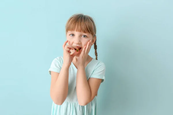 Malá holka brát rybí tuk pilulku na barevném pozadí — Stock fotografie