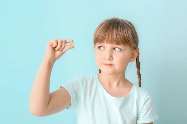 Malá holka s pilulkou rybího oleje na barevném pozadí — Stock fotografie