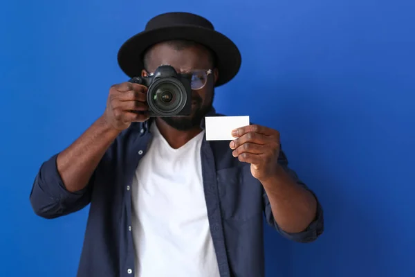 African-American photographer with camera and business card on color background — Stock Photo, Image