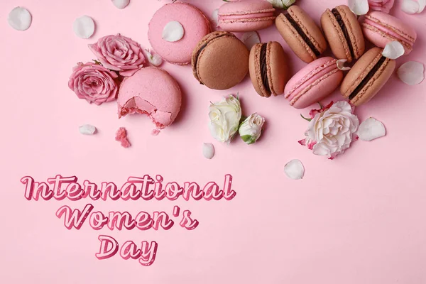 Different tasty macarons with flowers and text INTERNATIONAL WOMEN'S DAY on color background — Stok fotoğraf