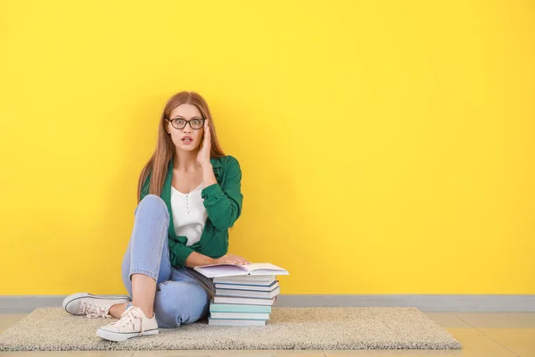 Mujer joven conmocionada con libros sentados cerca de la pared de color — Foto de Stock