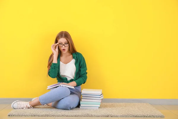 Verrast jonge vrouw met boeken zitten in de buurt kleur muur — Stockfoto