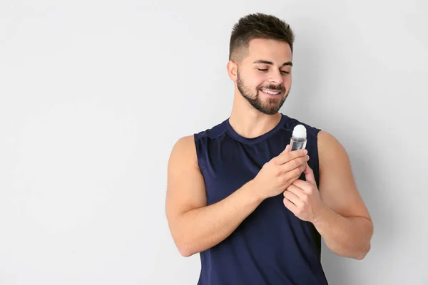 Handsome young man with deodorant on light background — Stock Photo, Image