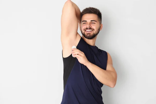 Handsome young man using deodorant on light background — Stock Photo, Image