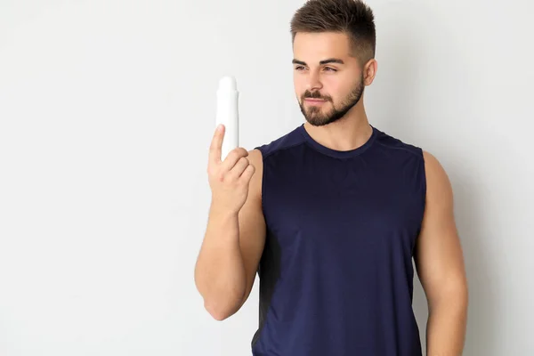 Handsome young man with deodorant on light background — Stock Photo, Image