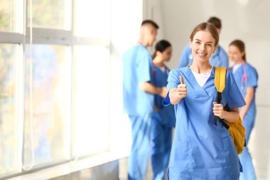 Female medical student showing thumb-up gesture in hall of clinic