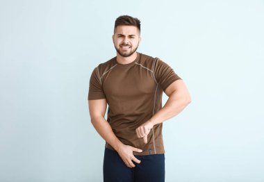 Young man with urologic disease showing thumb-down on light background