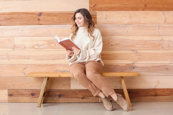 Hermosa mujer joven en suéter cálido libro de lectura cerca de la pared de madera — Foto de Stock