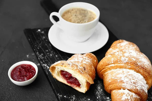Board with tasty sweet croissants, coffee and jam on dark background — Stockfoto