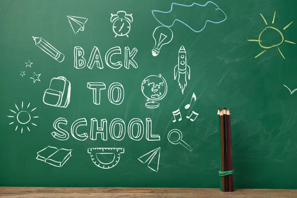 Pencils on table near blackboard with drawings and text BACK TO SCHOOL — Stock Photo, Image