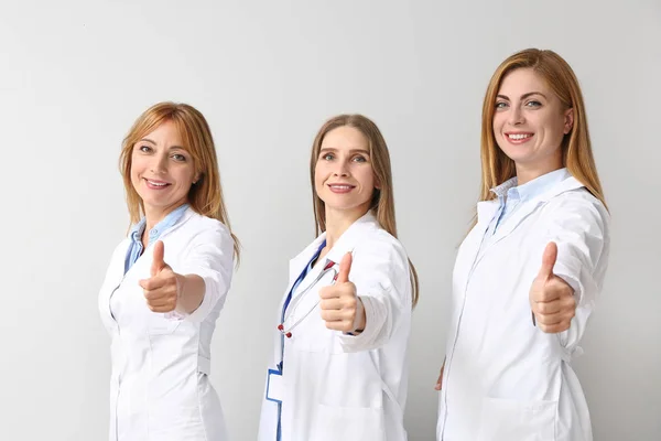Portrét ženských lékařek ukazující gesto palce nahoru na světlém pozadí — Stock fotografie