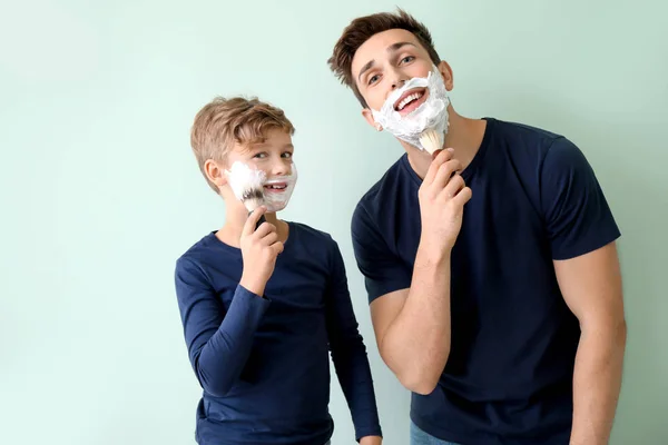 Father with son applying shaving foam onto their faces against grey background — Stock Photo, Image