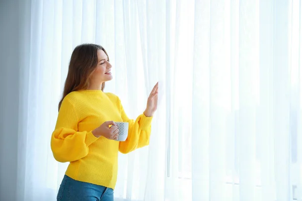 Mujer feliz con taza de té cerca de la ventana en casa — Foto de Stock