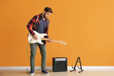 Young man playing guitar near color wall