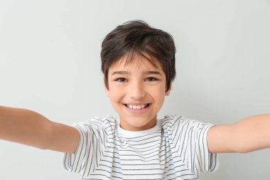 Cute little boy taking selfie on light background