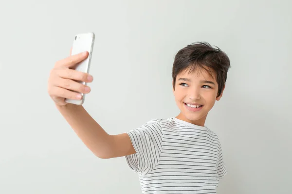 Cute little boy taking selfie on light background — Stock Photo, Image