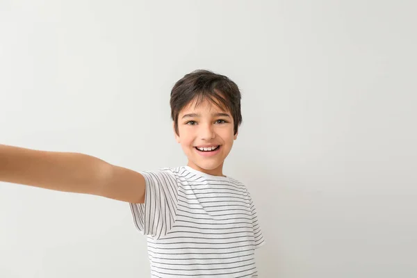 Netter kleiner Junge macht Selfie auf hellem Hintergrund — Stockfoto