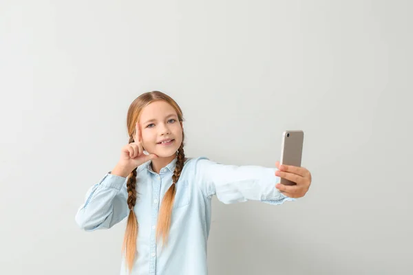 Cute little girl taking selfie on light background — Stock Photo, Image