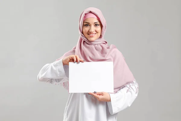 Young Arab woman with blank paper sheet on grey background — Stock Photo, Image