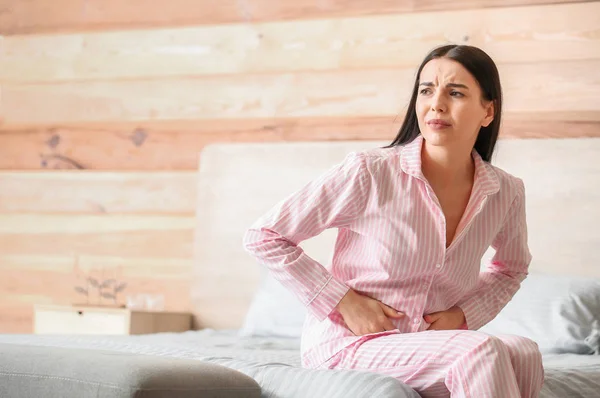 Mujer joven que sufre de calambres menstruales en el dormitorio — Foto de Stock