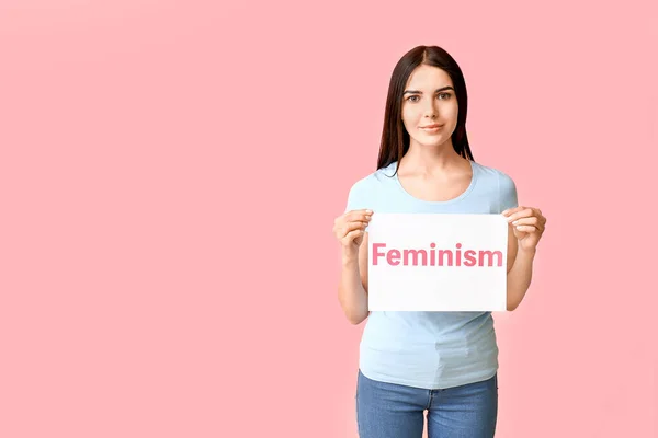 Jonge vrouw met papier met tekst Feminisme op kleur achtergrond — Stockfoto