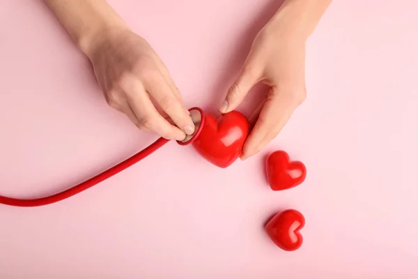 Vrouwelijke handen met rode harten en stethoscoop op kleur achtergrond. Cardiologie — Stockfoto