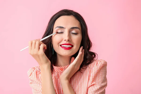 Bella giovane donna che applica il trucco su sfondo di colore — Foto Stock