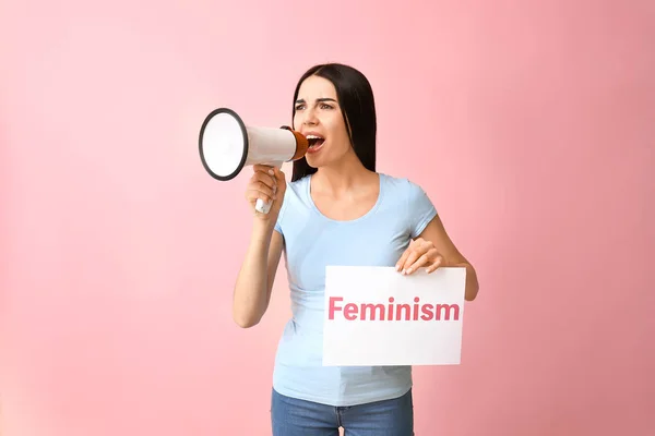 Mujer emocional con megáfono y papel con texto FEMINISMO sobre fondo de color. Concepto de feminismo — Foto de Stock