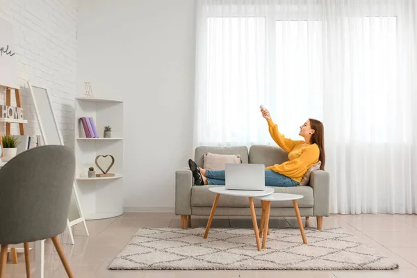 Young woman switching on air conditioner at home — Stock Photo, Image