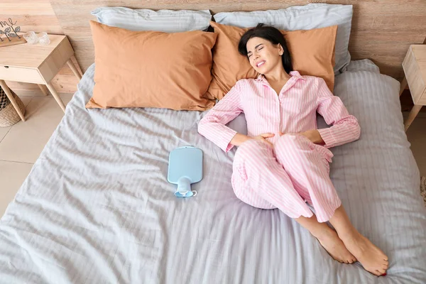 Mladá žena trpí menstruačními křečemi v ložnici — Stock fotografie