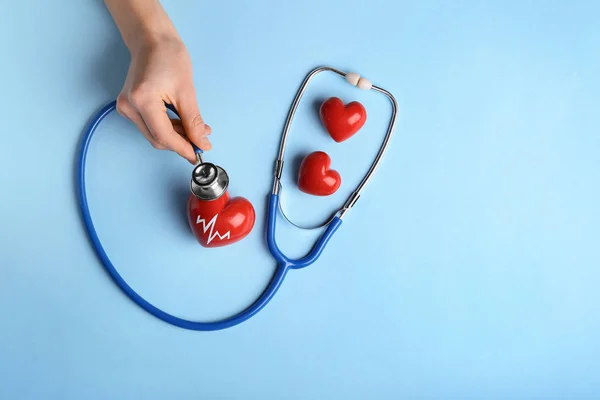 Mão feminina com corações vermelhos e estetoscópio sobre fundo de cor. Conceito de cardiologia — Fotografia de Stock