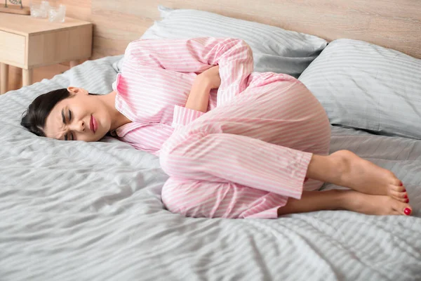 Молодая женщина страдает от менструальных спазмов в спальне — стоковое фото