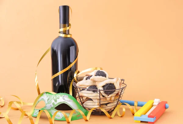 Tasty hamantaschen, gragger and party decor for Purim holiday and bottle of wine on color background — Stock Photo, Image
