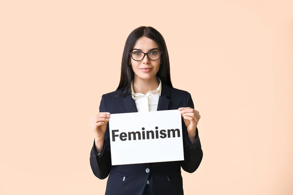 Jonge zakenvrouw met papier met tekst Feminisme op kleur achtergrond — Stockfoto