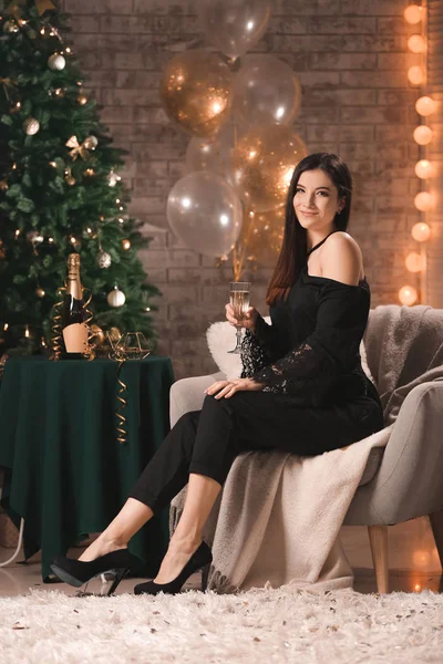 Beautiful young woman with champagne in room decorated for Christmas — Stock Photo, Image
