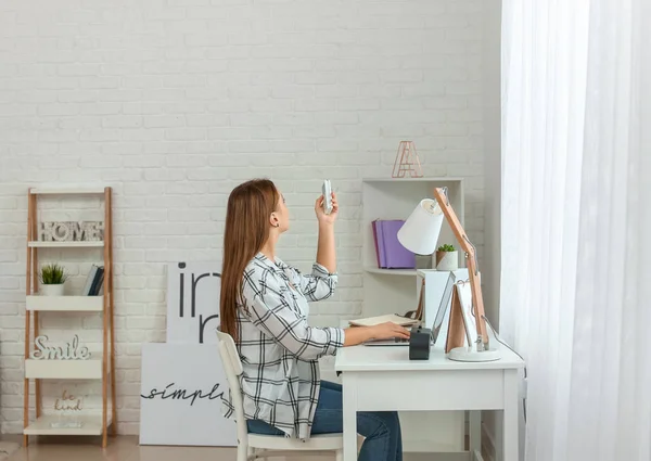 Young woman switching on air conditioner at home — Stock Photo, Image