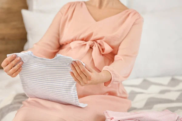 Pregnant woman with baby clothes in bedroom, closeup — Stock Photo, Image