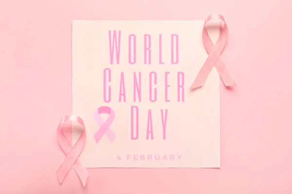 Pink ribbons and paper sheet with text WORLD CANCER DAY on color background