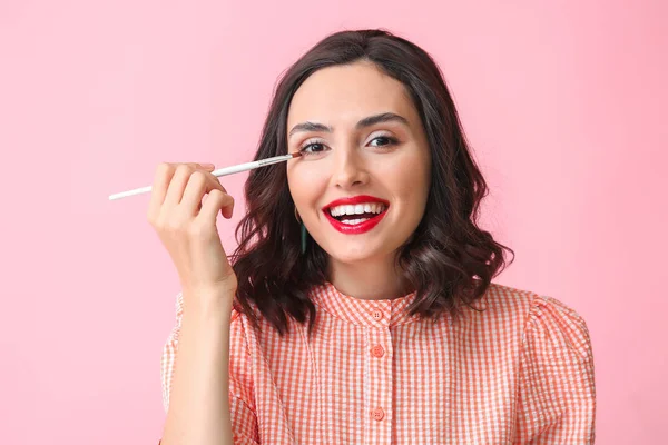 Krásná mladá žena použití make-up na barevném pozadí — Stock fotografie