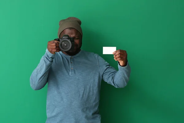 African-American photographer with camera and business card on color background — Stock Photo, Image