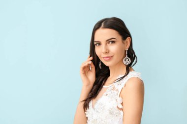 Young bride with beautiful jewelry on color background