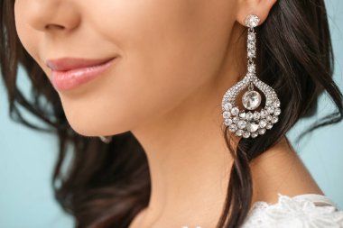 Young bride with beautiful jewelry on color background, closeup