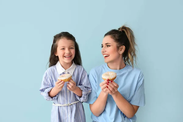 Bella giovane donna e bambina con ciambelle su sfondo di colore — Foto Stock