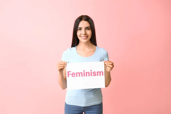 Jonge vrouw met papier met tekst Feminisme op kleur achtergrond — Stockfoto