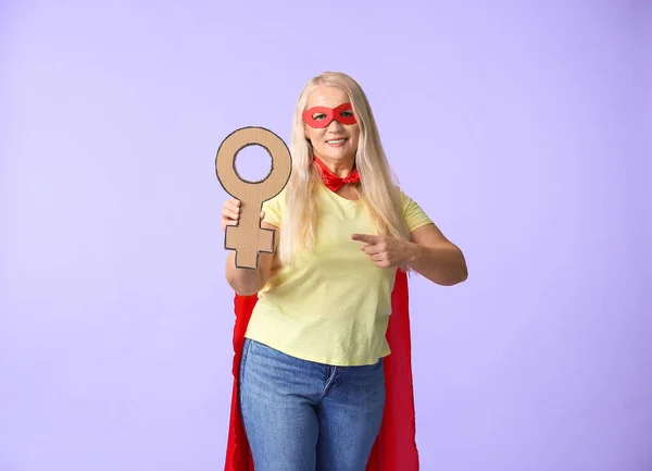 Lady in superhero costume holding symbol of woman on color background. Concept of feminism — Stock Photo, Image