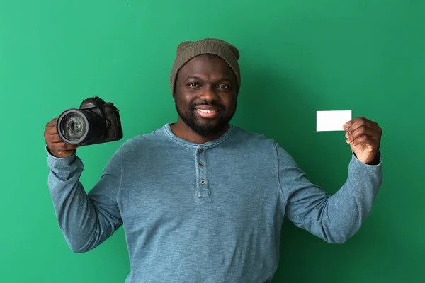 African-American photographer with camera and business card on color background — Stock Photo, Image