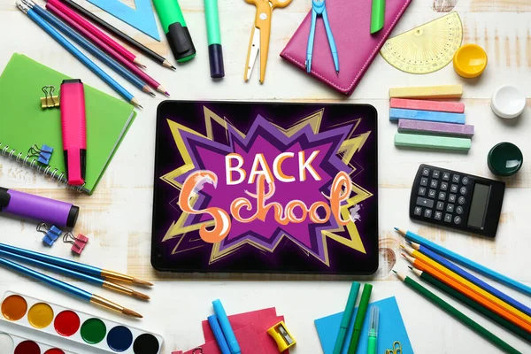 Tablet computer with text BACK TO SCHOOL on screen and stationery on wooden background — ストック写真