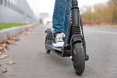 Teenage boy riding kick scooter outdoors, closeup